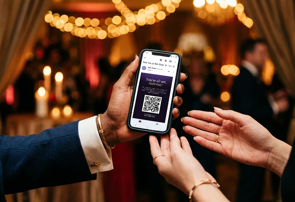 At a candlelit gala, a guest holds out a phone showing their confirmation email with a QR code for check-in